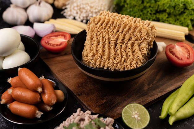 Noodles on a wooden cutting board with tomato, lime, spring onion, chili and baby corn