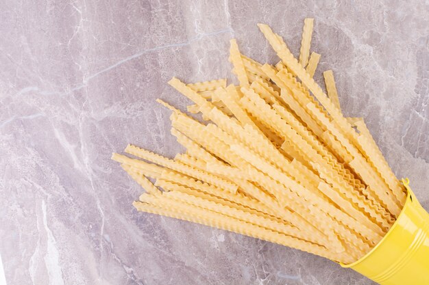 Noodles in a yellow metallic bucket on grey surface