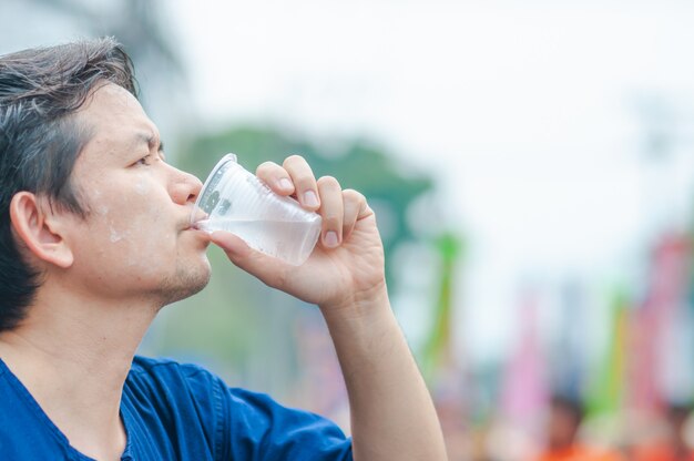 Northern Thai man drink fresh cold water in plastic glass during participation outdoor activity 