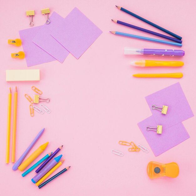Note papers; color pencils and paper clips over pink backdrop
