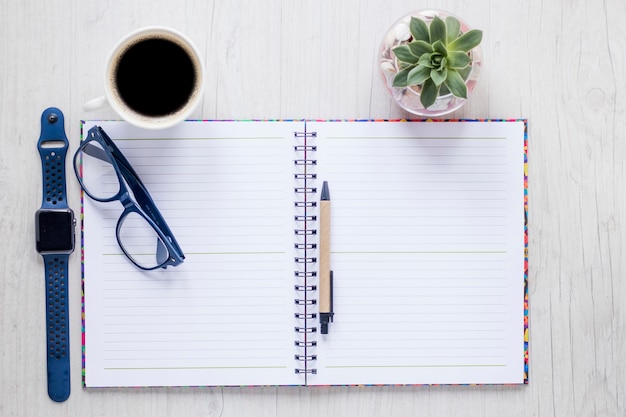 Notebook and accessories near coffee and plant