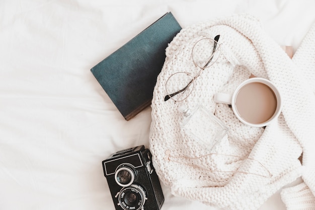 Notebook and camera near sweater with things on bedsheet