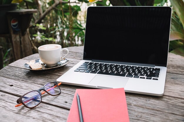 Notebook and glasses near laptop and cup