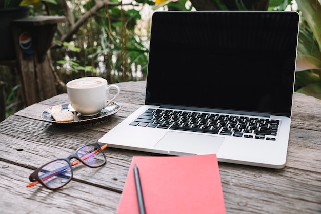 Notebook and glasses near laptop and cup