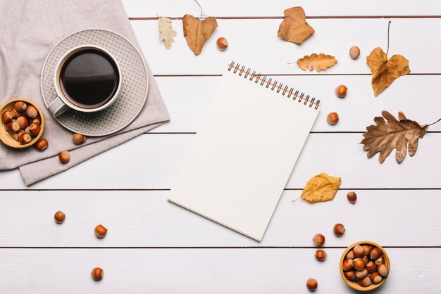 Notebook and leaves near coffee and nuts