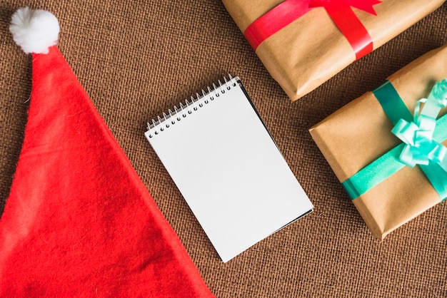 Notebook near Christmas hat and present boxes