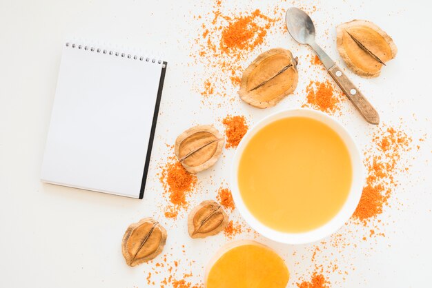 Notebook near foliage pepper and orange liquid