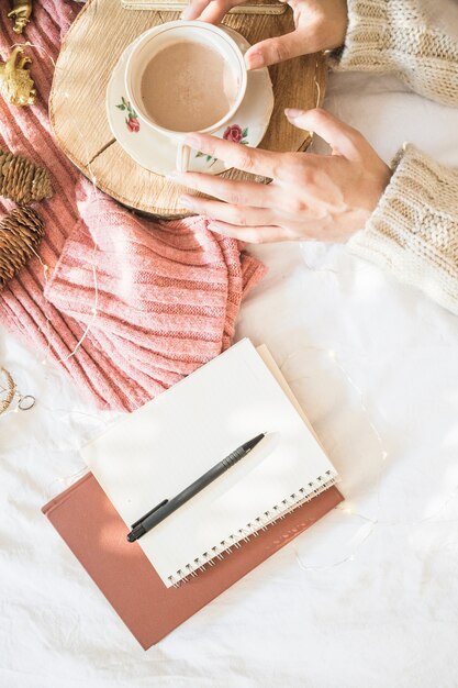 Notebook and pen near hands with beverage