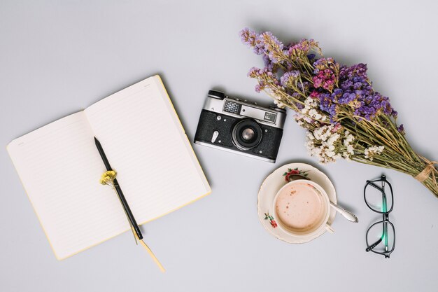 Notebook with camera and flowers on table