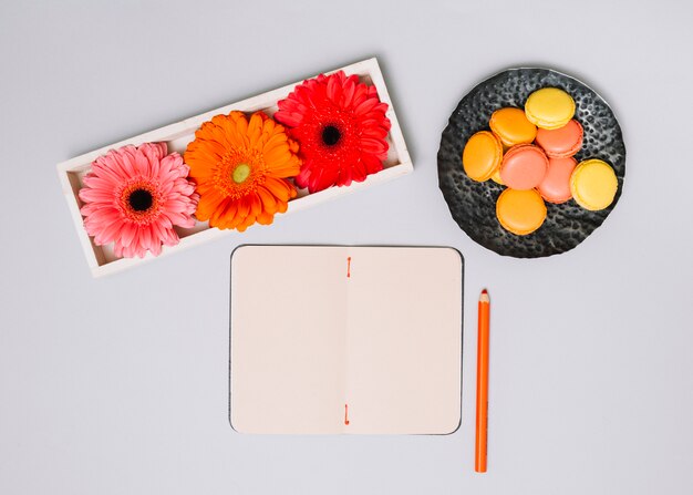 Notebook with cookies and bright flowers on white table