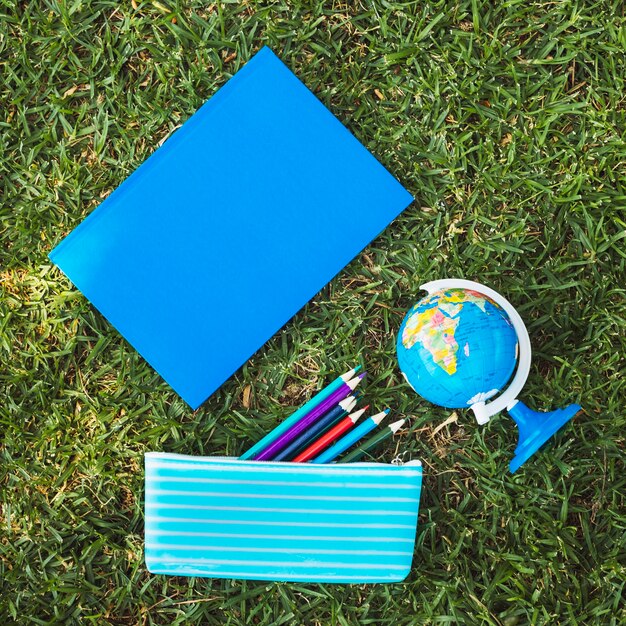 Notebook with globe and pencil case on grass