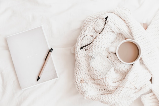 Notebook with pen on it near sweater with things on bedsheet