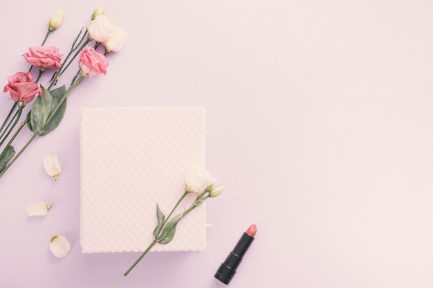 Notebook with rose flowers and lipstick on table