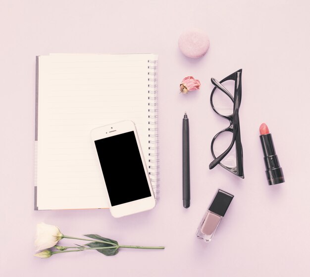 Notebook with smartphone, flower and cosmetics on table