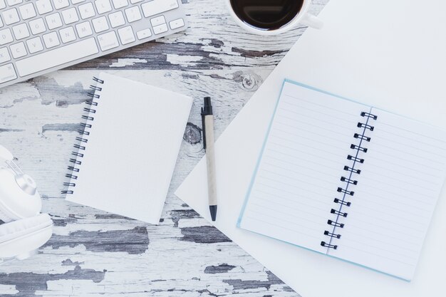 Notebooks and headphones near keyboard and coffee cup on grungy desk