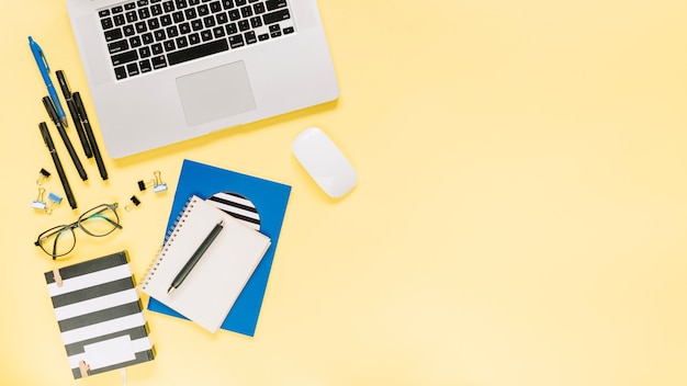 Notebooks and laptop with stationeries on colored backdrop