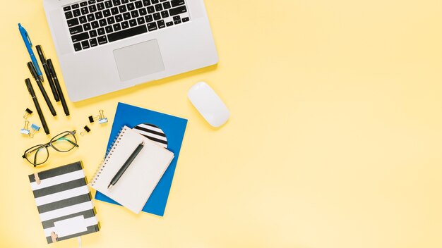 Notebooks and laptop with stationeries on colored backdrop