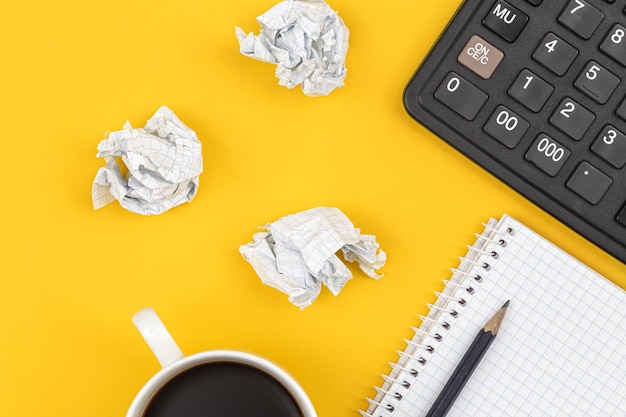 Notepad calculator coffee cup and crumpled paper balls on a yellow background