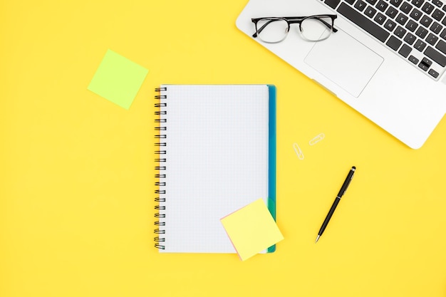 Free photo notepad laptop and glasses on a yellow background top view