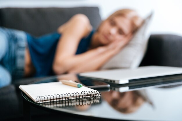 ソファで寝ている女性の近くのテーブルの上のメモ帳とラップトップ
