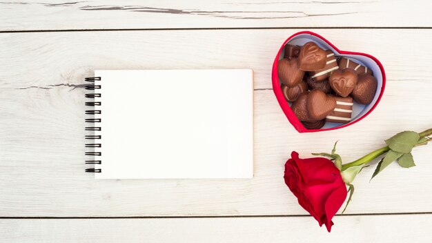 Notepad near box with sweets and flower