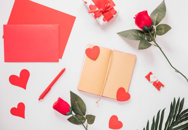 Блокнот рядом с бумагами, орнаментом сердечками, цветами, ручкой и подарком