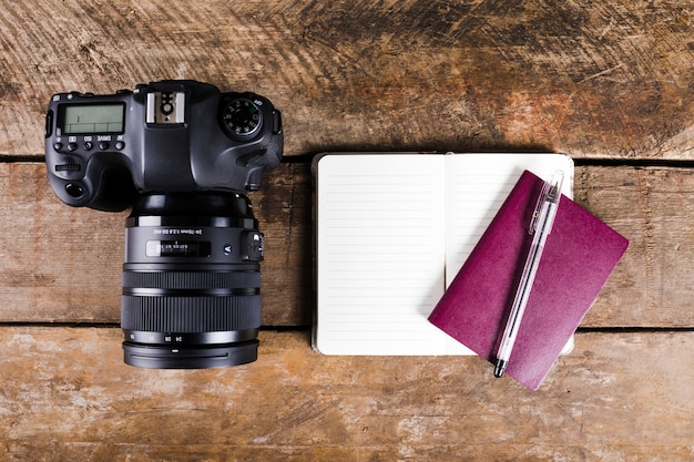 Блокнот, паспорт, ручка и зеркальная фотокамера на деревянном фоне
