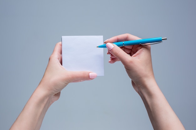 notepad and pen in female hands on gray background
