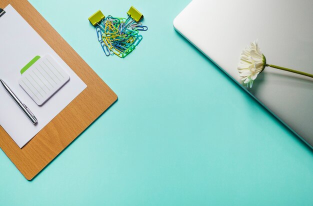 メモ帳。ペン;緑の背景にpaperclipsとラップトップとクリップボード上の紙