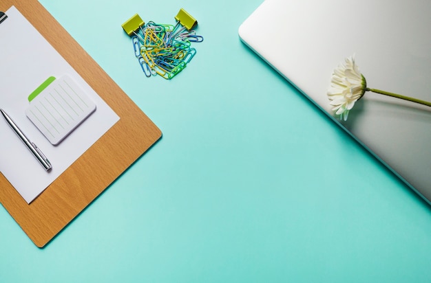 Блокнот; ручка; бумага в буфер обмена с скрепками и ноутбук на зеленом фоне