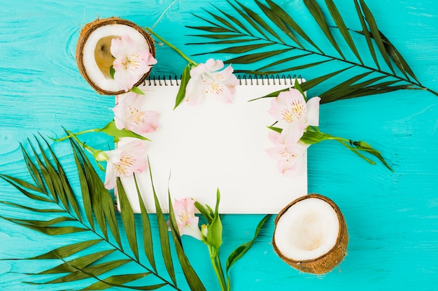 Notepad among plant leaves with fresh coconuts and blooms