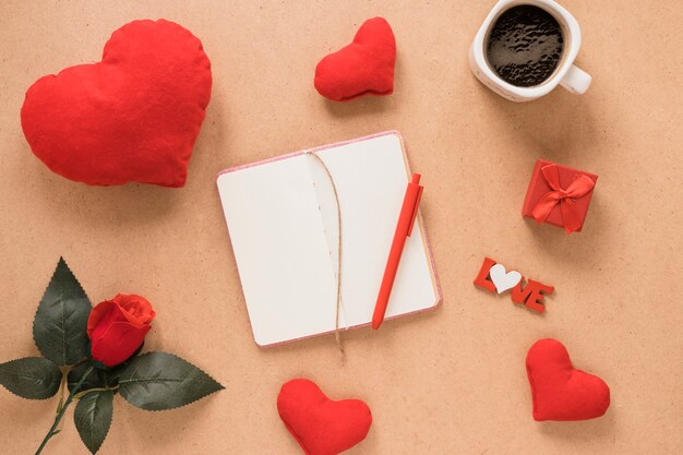 Notepad with pen near ornament hearts, flower and cup of drink