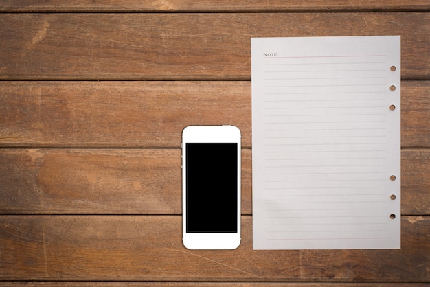 Notepad with smart phone on office wooden table.