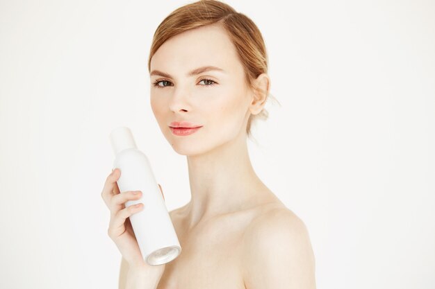 Nude beautiful blonde girl with fresh perfect skin smiling holding cosmetology spray bottle .