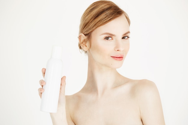 Nude beautiful blonde girl with fresh perfect skin smiling holding cosmetology spray bottle .