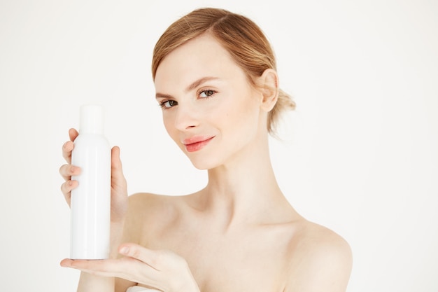 Nude beautiful blonde girl with fresh perfect skin smiling holding cosmetology spray bottle .