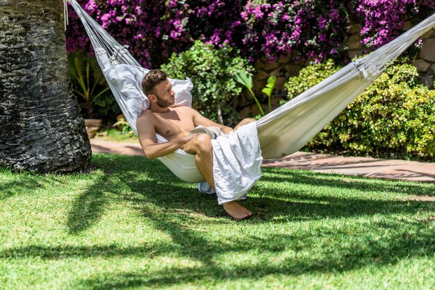 nude male relaxing in a hammock in the garden.