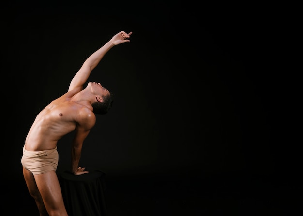 Nude man leaning on chair with hand and pulling up 