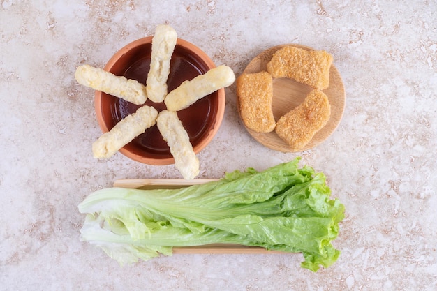 Foto gratuita pepite, bastoncini di formaggio e foglie di lattuga a terra.