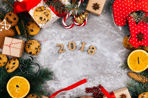 Number 2018 lies in the center of a circle made of oranges, cookies, fir branches, red present boxes and other kinds of Christmas decor