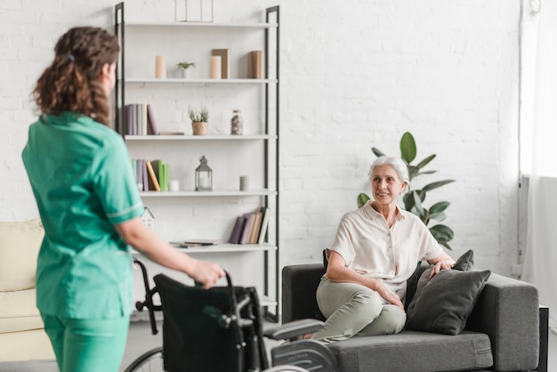 Nurse bringing wheelchair to her senor female patient sitting on couch