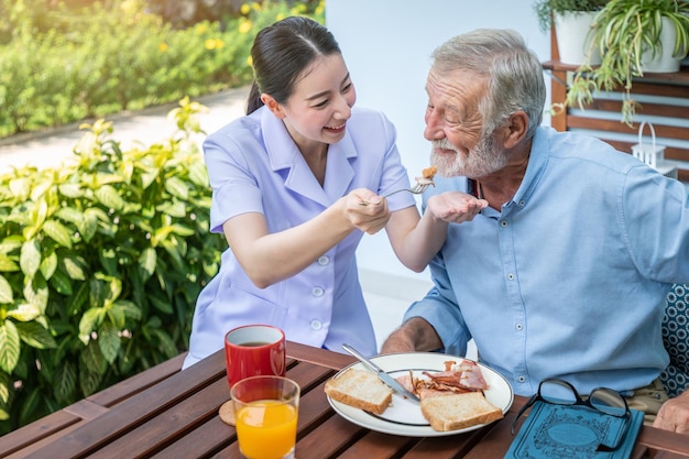 Nurse feeding elderly senior man to eat breakfast at nursing home