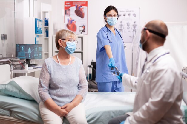 Nurse giving doctor senior patient x-ray wearing face mask as safety precaution in the course of covid19 outbreak