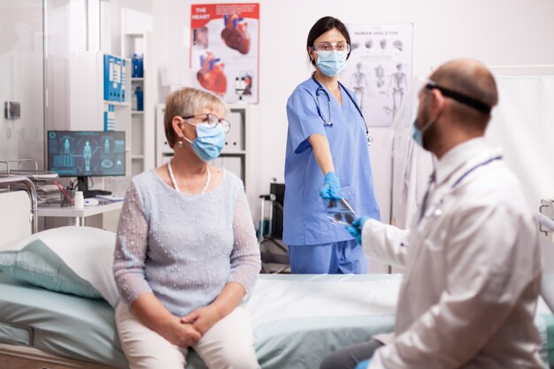 covid19の発生時に安全対策としてフェイスマスクを着用したシニア患者のX線写真を医師に与える看護師