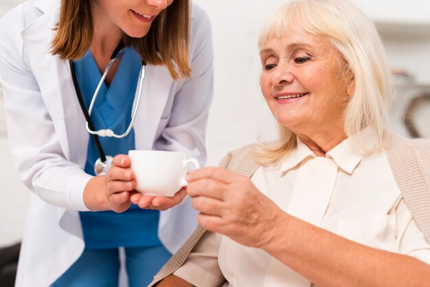 Медсестра дает чай пожилой женщине крупным планом