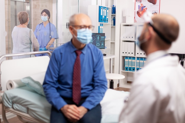 Nurse in hospital corridor discussing with handicapped senior woman with walking frame