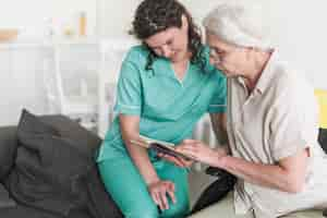 Free photo nurse looking at senior woman reading book