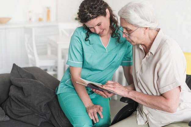 Nurse looking at senior woman reading book