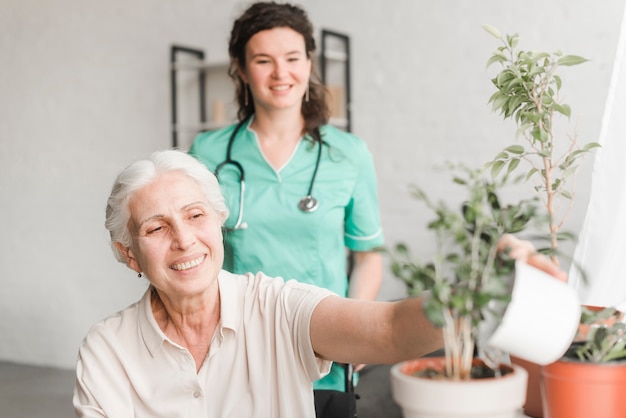 Nurse looking at senior woman sitting in wheelchair watering the plant