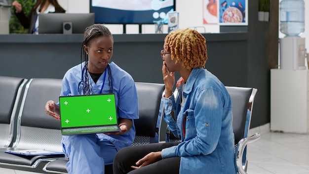 Nurse and patient looking at laptop with greenscreen display, consulting in waiting room reception. Analyzing isolated mockup template with blank chromakey copyspace background.